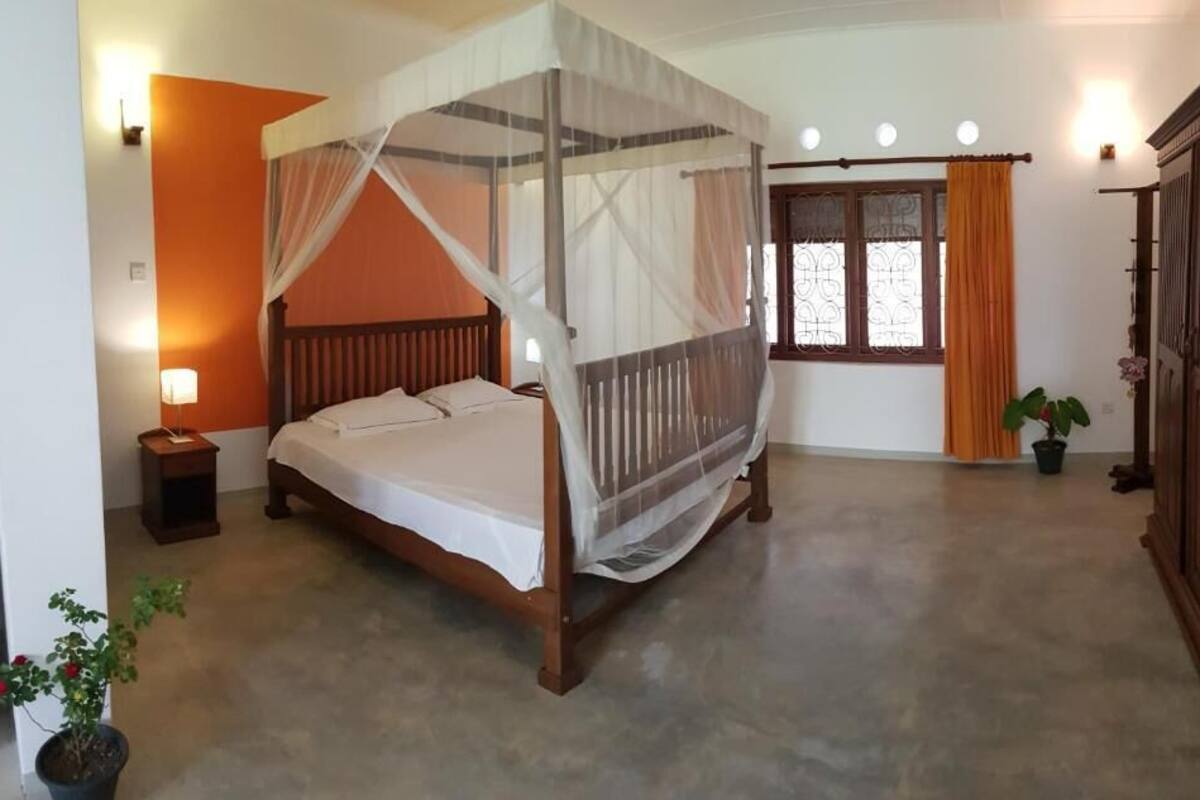 A bedroom with a four-poster bed, a nightstand, a potted plant, and a wardrobe.