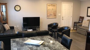 Ein Wohnzimmer mit Esstisch, Stühlen, einer Couch, einem Fernseher und einem Poster an der Wand.
