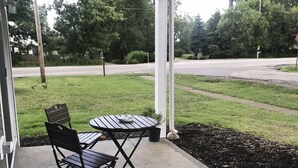 Eine überdachte Terrasse mit Tisch und Stühlen, einem Betonboden und Blick auf eine Straße und Grünflächen.