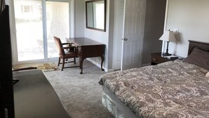 Ein Schlafzimmer mit Bett, Schreibtisch, Stuhl, Fernseher und einer Tür, die auf einen Balkon führt.