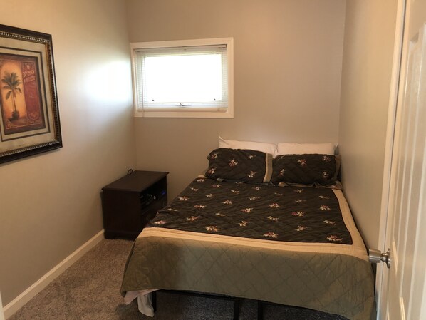 A small bedroom with a bed, a nightstand, a framed picture on the wall, and a window.