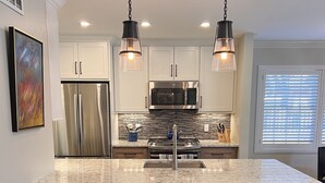 A modern kitchen with a large island, stainless steel appliances, and pendant lighting.