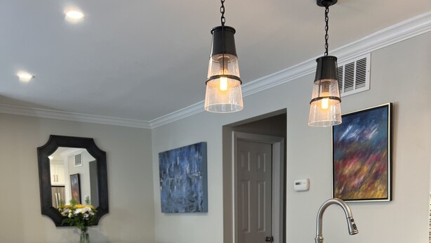 A kitchen with a granite countertop, wooden cabinets, a stainless steel sink, and pendant lighting.