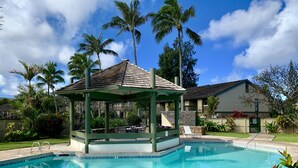 Ein Swimmingpool mit einer Laube, Palmen und einem Haus im Hintergrund.
