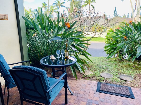 A patio area with a round glass table, two chairs, a bottle of wine, and a decorative shell.