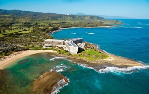 An aerial view of a coastal resort with a large building, beachfront, and clear blue waters.