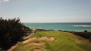 Luftaufnahme eines Golfplatzes mit Bunkeranlagen, blauem Himmel und dem Meer im Hintergrund.