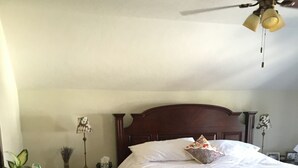 Een slaapkamer met een houten bed, een plafondventilator, een nachtkastje met een lamp en een kleine tafel met een plant.