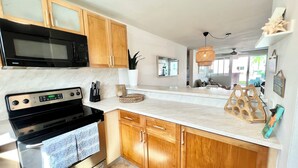 A modern kitchen with wooden cabinets, a black microwave, a stainless steel stove, and a white countertop. - Beach Oasis - Ground Floor Beach Apartment Steps to the Pool! (Río Grande)