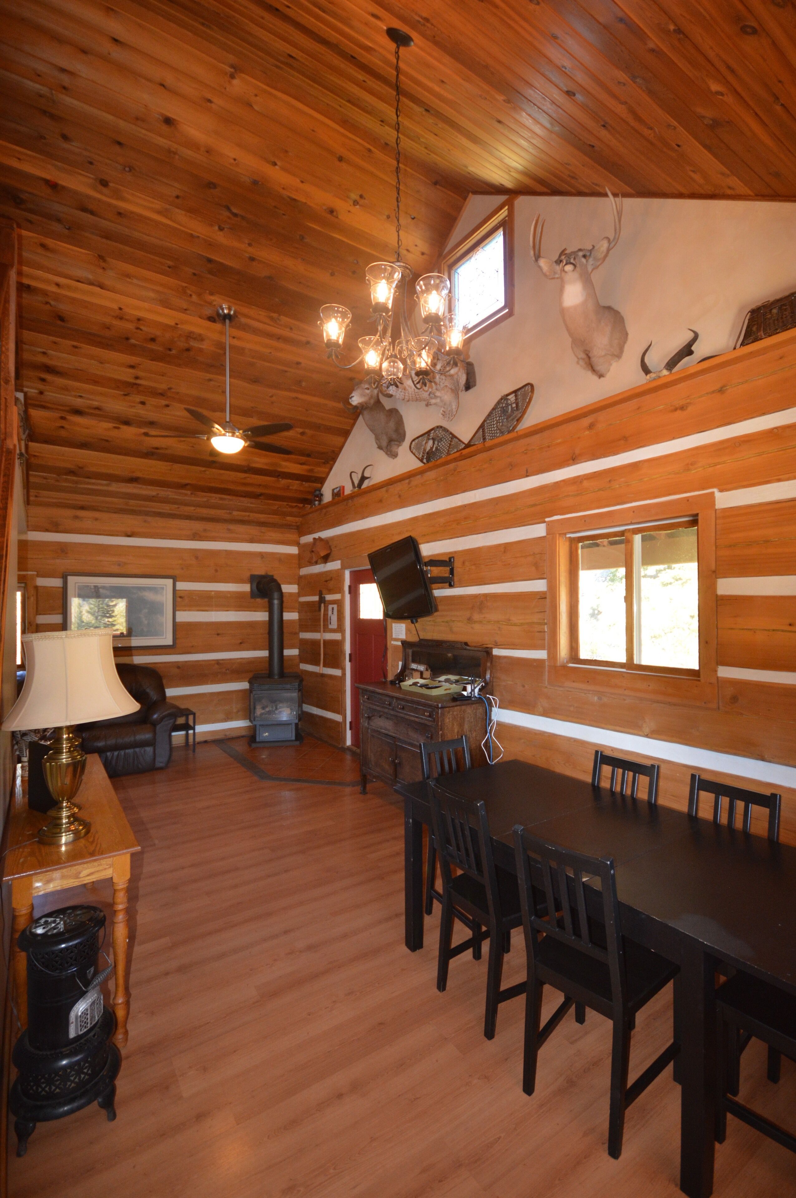 A log cabin interior with a dining area, fireplace, and mounted animal heads on the wall.
