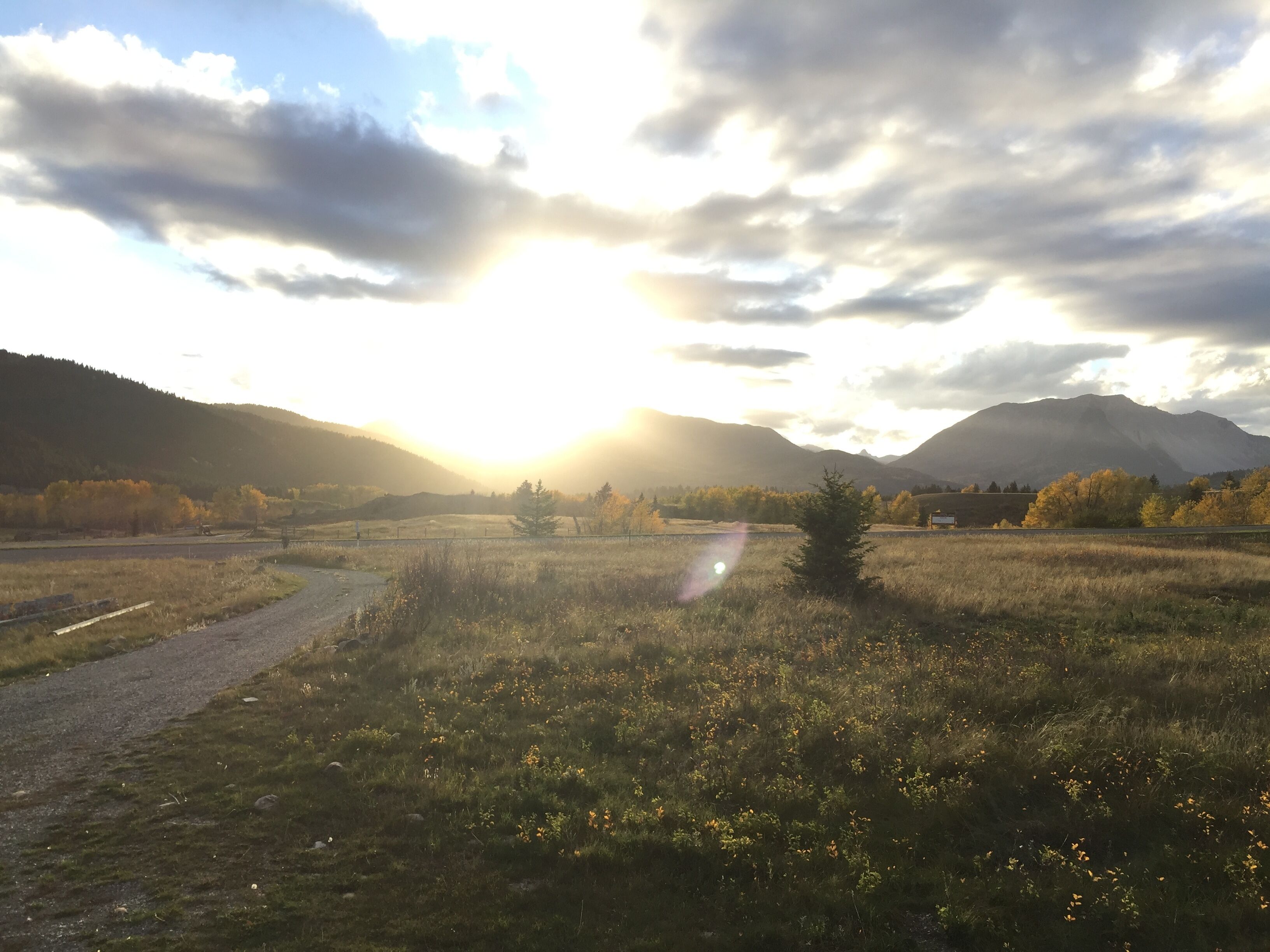 A rural landscape with a dirt path, fields, and mountains in the background.