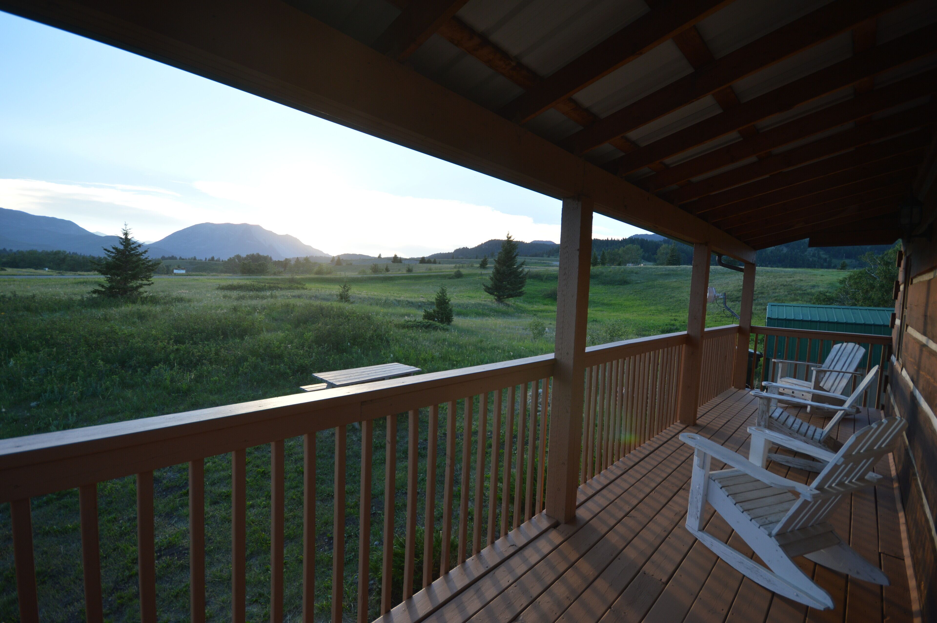 Eine Holzterrasse mit weißen Schaukelstühlen mit Blick auf ein Grasfeld und Berge.