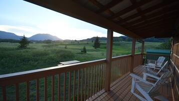 Eine Holzterrasse mit weißen Schaukelstühlen mit Blick auf ein Grasfeld und Berge.
