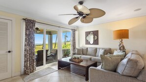 A living room with a ceiling fan, a sofa, a coffee table, and a view through a glass door to the outdoors. - 616 Surf Villas, Oceanfront Condo, BAM Vacation Rentals (Ponte Vedra Beach)