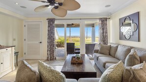 A living room with a sofa, coffee table, and a ceiling fan. There is a door leading to a balcony with a view of the outdoors. - 616 Surf Villas, Oceanfront Condo, BAM Vacation Rentals (Ponte Vedra Beach)