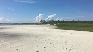 Ein sandiger Strand mit Fußabdrücken, einem klaren Himmel und einer Baumreihe in der Ferne.