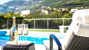 Une bouteille de champagne, deux verres et un plateau sur une table près d’une piscine, avec vue sur des collines et des maisons.