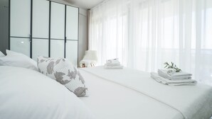 Une chambre moderne avec un grand lit, une armoire et une fenêtre ornée de rideaux légers.
