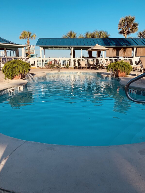 Relax by the serene pool surrounded by palm trees and lounge chairs.
