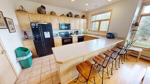 A modern kitchen with a large island, bar stools, and a view of the outdoors through a window. - Big End Unit, Deck! Near Lake Trail. Easy Drive to Dining, Activities, Events (Frisco)