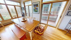 A dining area with a wooden table, chairs, and a bench. There are large windows and a view of a balcony. - Big End Unit, Deck! Near Lake Trail. Easy Drive to Dining, Activities, Events (Frisco)