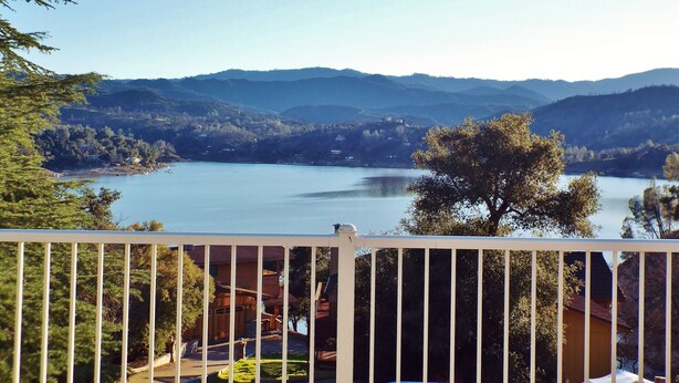 A lakeside view with a wooden house and a white fence in the foreground. - Wow! 2 Master Suites, Lake Naci Views, WiFi, and Private Slip! (Lake Nacimiento)