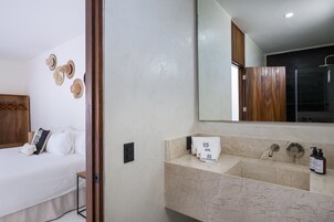 Habitación de hotel con cama, baño con lavamanos de mármol y espejo que refleja la habitación.