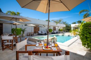 Un coin petit-déjeuner aménagé au bord de la piscine, avec des tables, des chaises et des parasols.