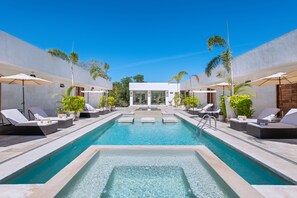 A pool area with lounge chairs and umbrellas, surrounded by palm trees and a clear blue sky. - Avela Boutique Hotel (Sayulita)