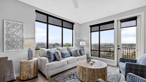 Un salon moderne avec un canapé gris, une table basse ronde et une vue sur la ville grâce à de grandes fenêtres.