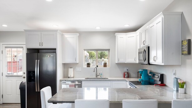 Una cocina moderna con armarios blancos, un refrigerador negro, un fregadero y una cafetera azul.