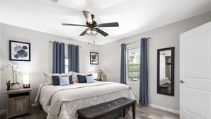Un dormitorio con cama, una banca, una mesita de noche, un ventilador de techo y una puerta.