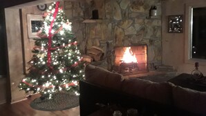 Ein gemütliches Wohnzimmer mit Kamin aus Stein, einem Weihnachtsbaum und einer komfortablen Sitzecke.