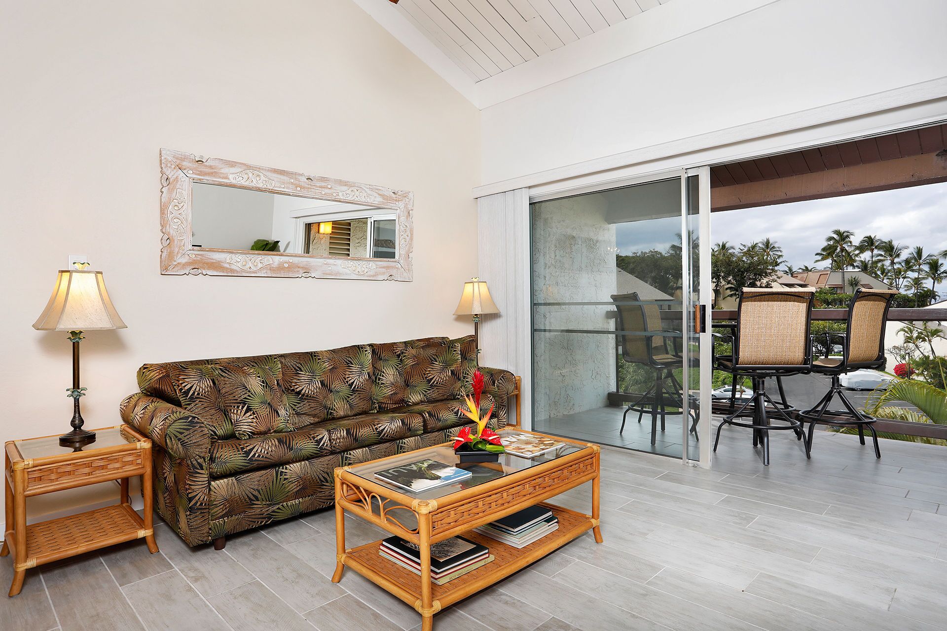 A living room with a sofa, two side tables with lamps, a glass coffee table, and a large mirror on the wall.