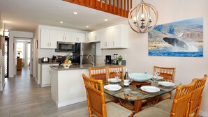 Una cocina moderna con armarios blancos, electrodomésticos de acero inoxidable y un comedor con mesa de vidrio y sillas de mimbre.