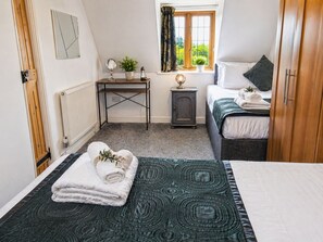 Ein Schlafzimmer mit einem Bett, einem Nachttisch mit Lampe, einem kleinen Tisch mit Spiegel und Pflanze sowie einem Fenster mit Vorhängen.