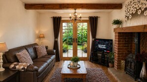 Un salon avec un canapé en cuir, une table basse, un téléviseur, une cheminée et une porte donnant sur un jardin.