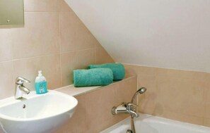 A bathroom with a sink, a bottle of hand soap, and a bathtub.