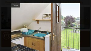 Een keuken met een blauwe spoelbak, houten kasten en uitzicht op een groen gazon door een balkondeur.