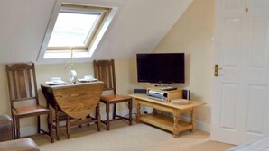 Een gezellige kamer met een schuine kap, een eettafel met stoelen, een televisie en een deur.
