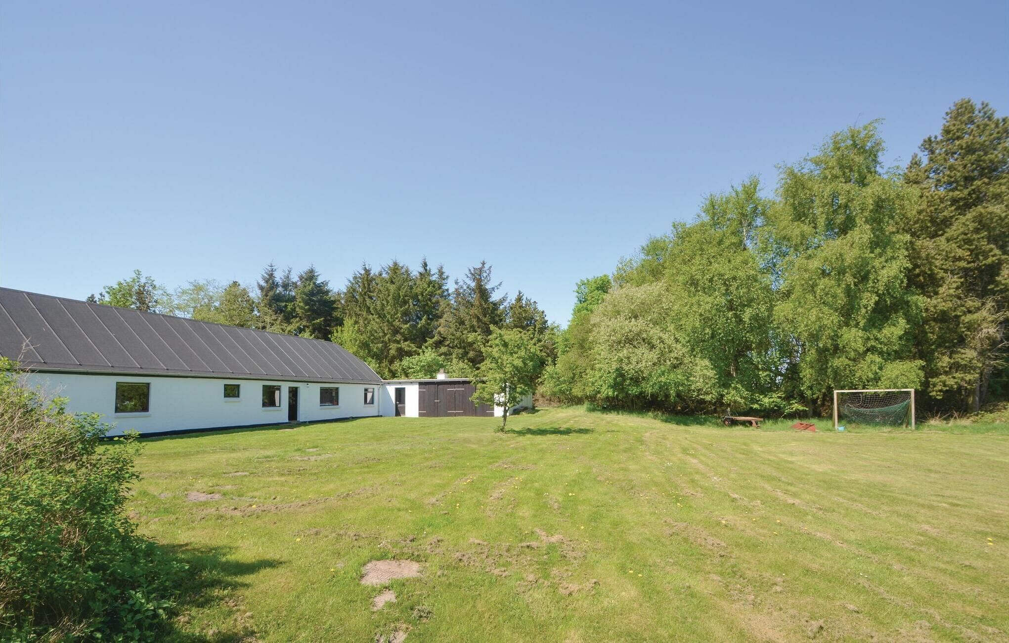 A residential property with a large grassy yard, a house with a sloped roof, and a fenced area with a goal post.
