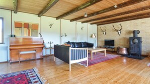 Ein geräumiges Wohnzimmer mit Holzboden, einem Klavier, einer Couch, einem Fernseher und einem Kamin.