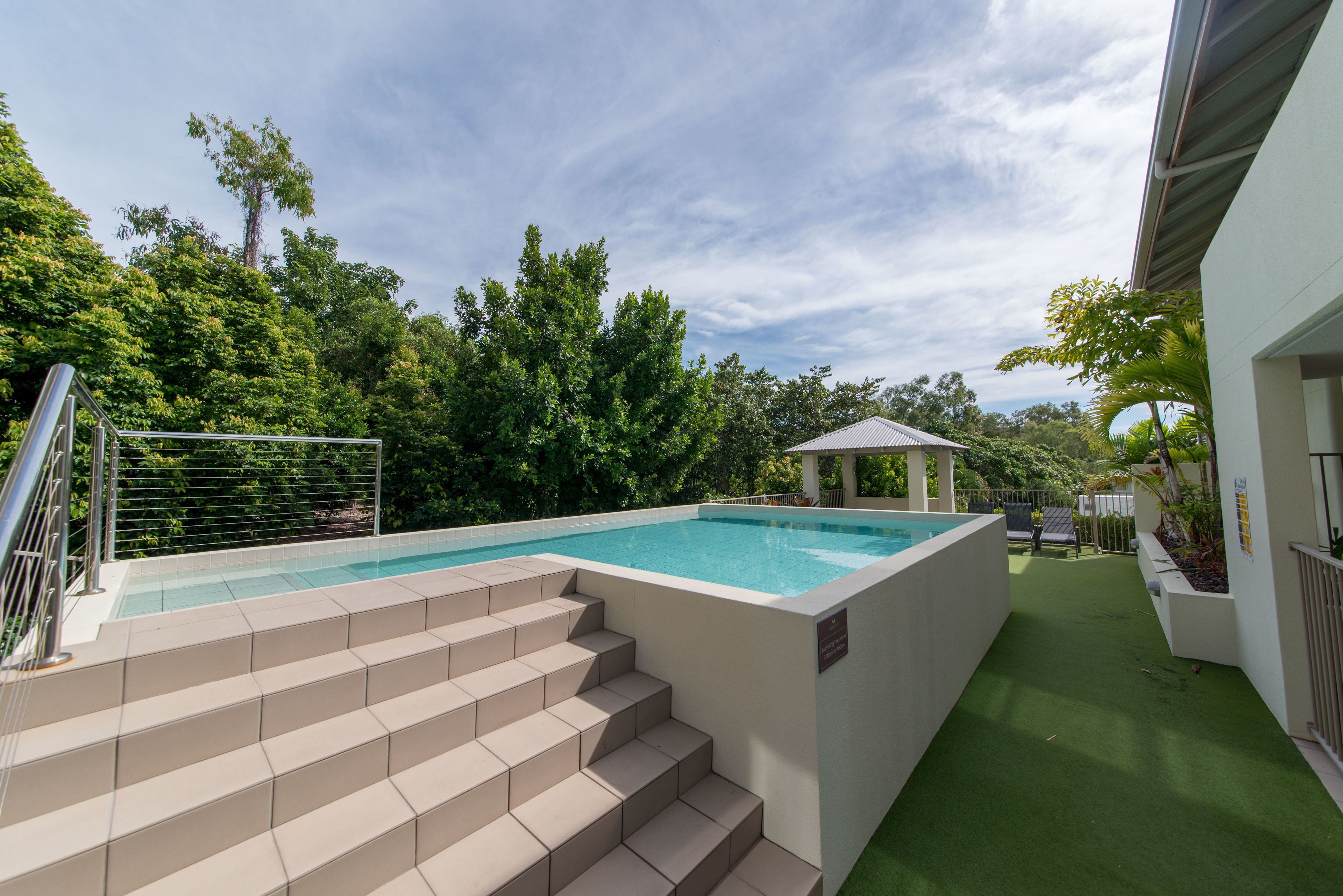 A swimming pool with steps leading up to it, surrounded by greenery and a covered seating area.