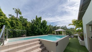 Una piscina con escalones de acceso, rodeada de vegetación y un área de descanso cubierta.