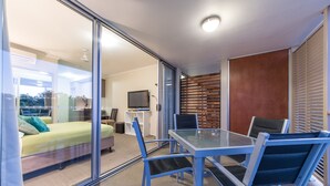 Una habitación moderna con un separador de vidrio, una cama, un televisor y una zona de comedor con sillas y una mesa.
