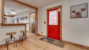 Un couloir avec une porte rouge, un plancher en bois et deux tabourets.