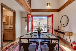 Un comedor con una mesa dispuesta para cuatro, techo de madera y vistas a montañas a través de puertas abiertas.