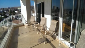 Ein Balkon mit vier Stühlen, großen Fenstern und Blick auf eine Stadtlandschaft.