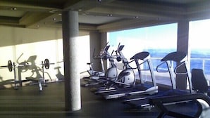 Ein Fitnessstudio mit verschiedenen Trainingsgeräten, darunter Laufband, Ergometer und eine Gewichtshalterbank.