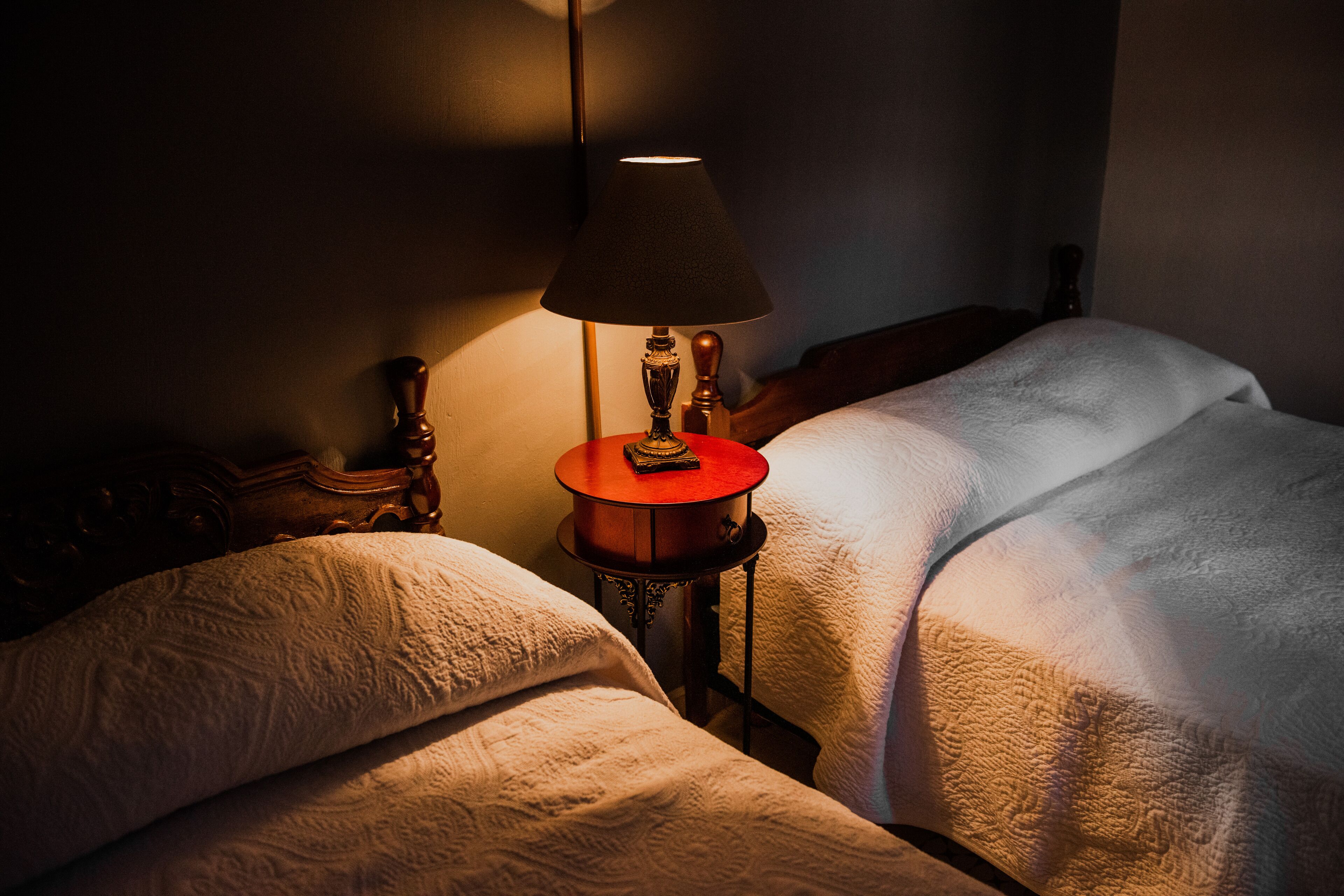 A hotel room with two beds, a nightstand with a lamp, and a wooden headboard.